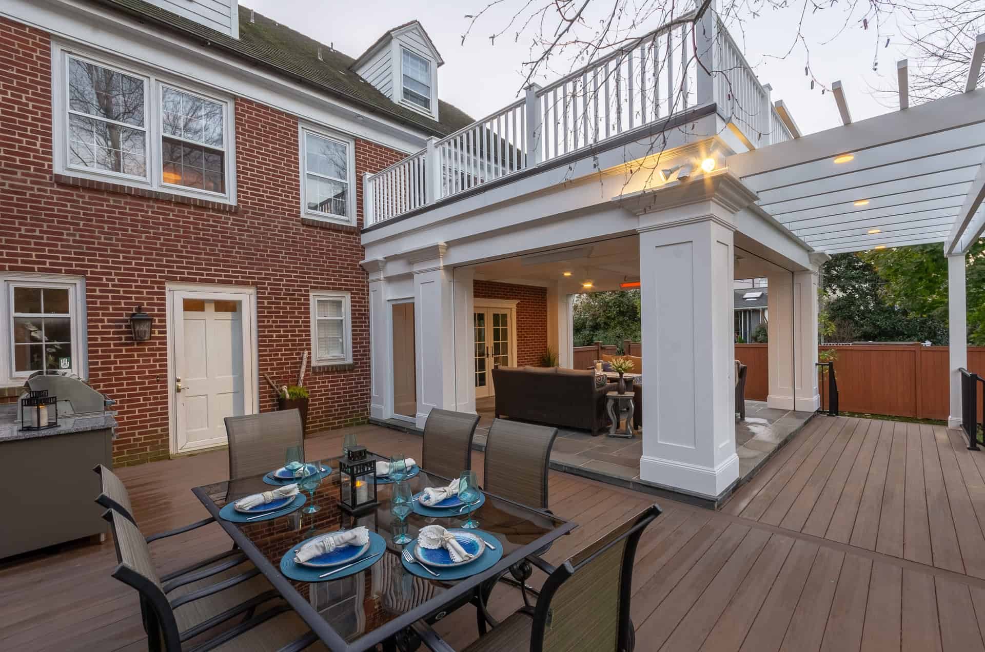 Covered deck with outdoor dining, seating area, and upper balcony attached to brick home in Delaware County, PA
