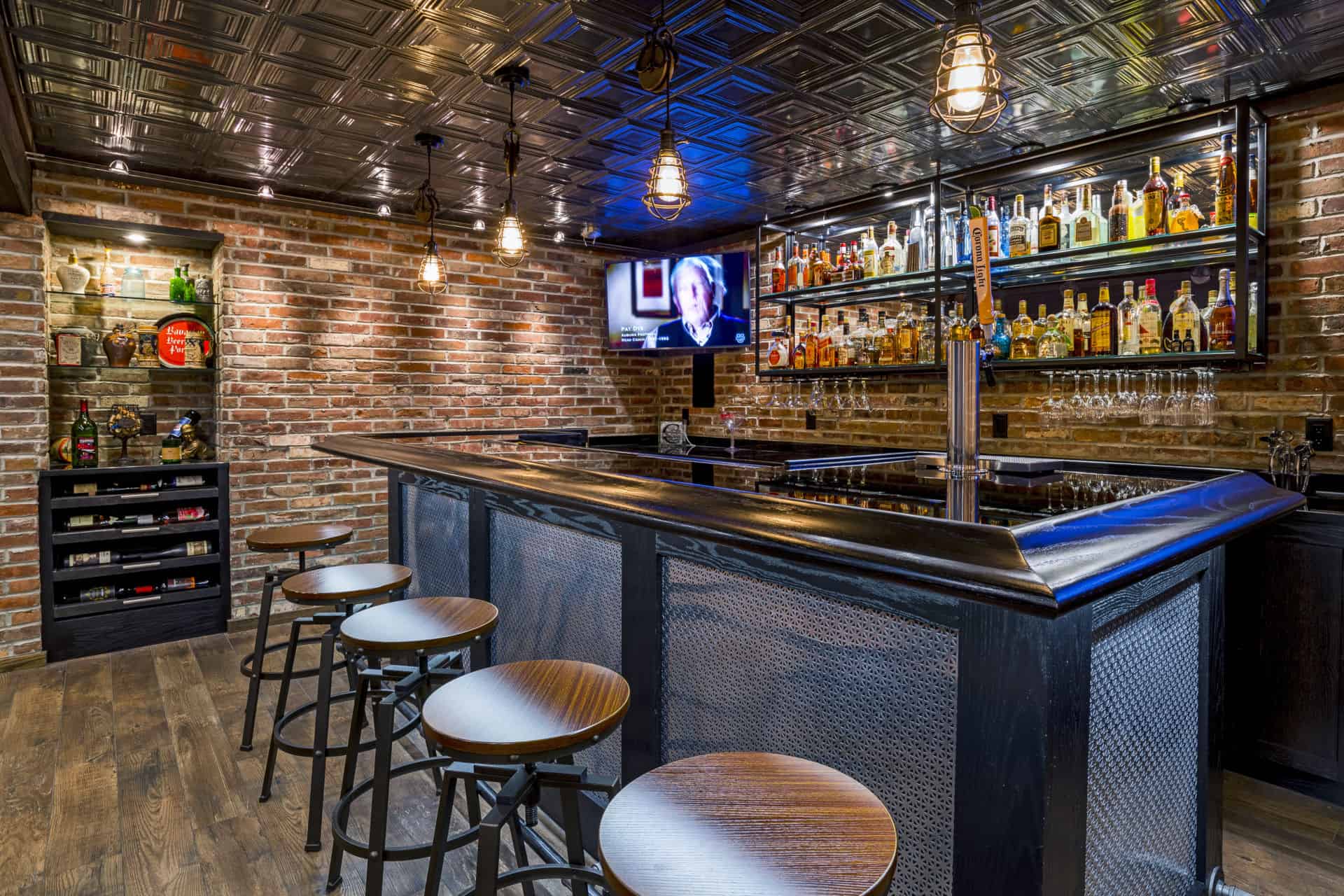 Industrial-style basement bar with brick walls, metal ceiling, liquor shelves, and stools in Delaware County, PA