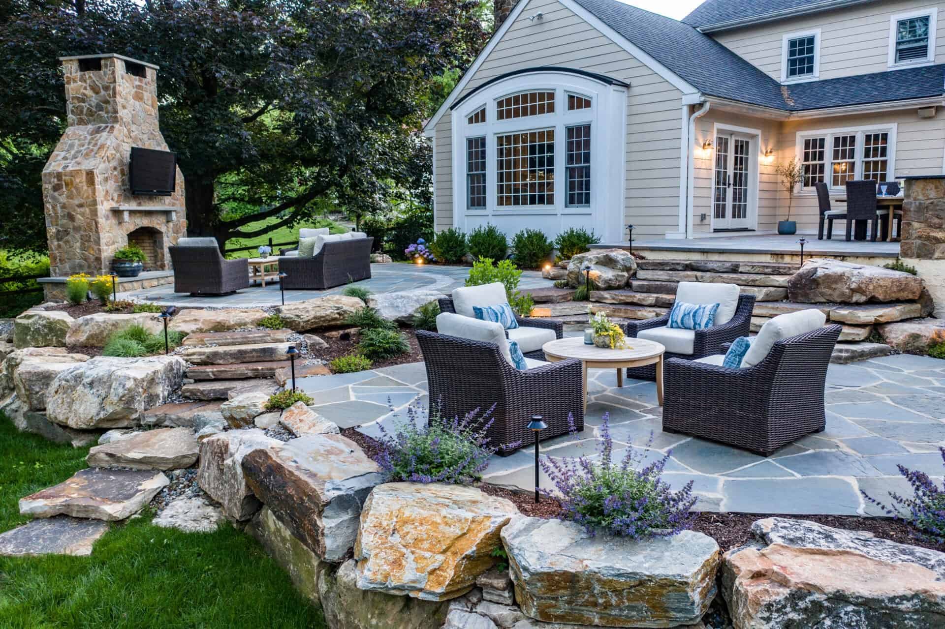 Tiered stone patio with outdoor seating, fireplace, and landscaped garden in Delaware County, PA