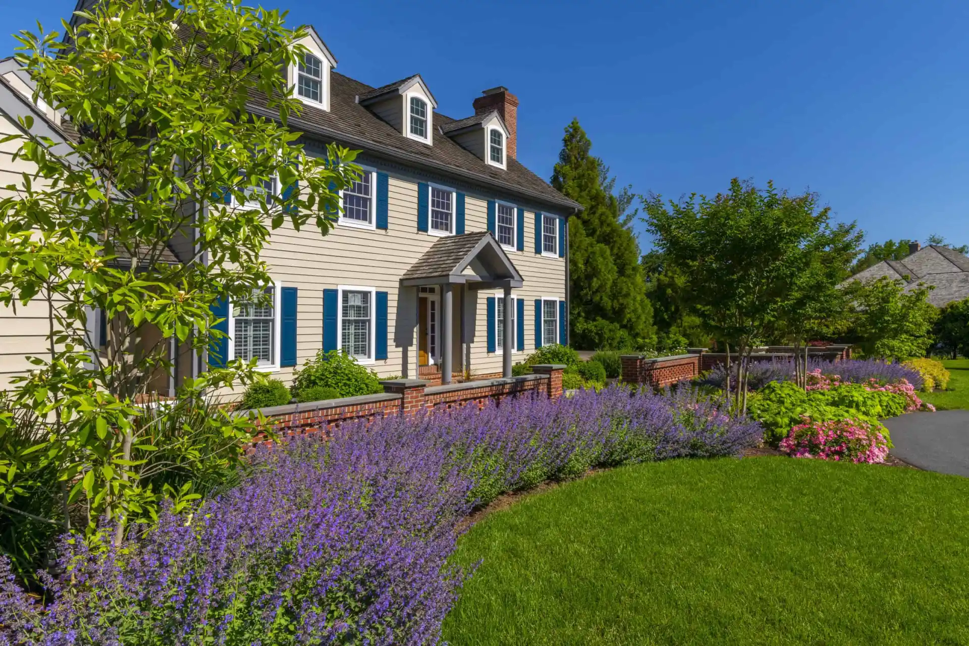 This charming two-story house, with beige siding and blue shutters, is nestled in lush greenery
