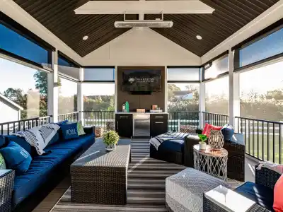 Stylish sunroom with dark wicker furniture, blue cushions, and a striped rug sets the stage for outdoor living in Delaware County, PA. Large windows offer scenic views and ample natural light. A small table with decorative items and plants completes the cozy space.