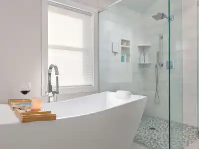 Modern bathroom with a freestanding bathtub featuring a bamboo tray holding a lit candle, glass of red wine, and book. Adjacent is a sleek, glass-enclosed shower. Complementing your indoor oasis, explore outdoor living in Delaware County PA for a complete at-home retreat experience.
