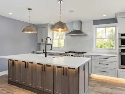 Modern kitchen with a large island featuring dark wood cabinets and a white marble countertop. Two pendant lights hang above. Gray cabinets, stainless steel appliances, and a herringbone backsplash complete the space, blending indoor elegance seamlessly with outdoor living in Delaware County PA.