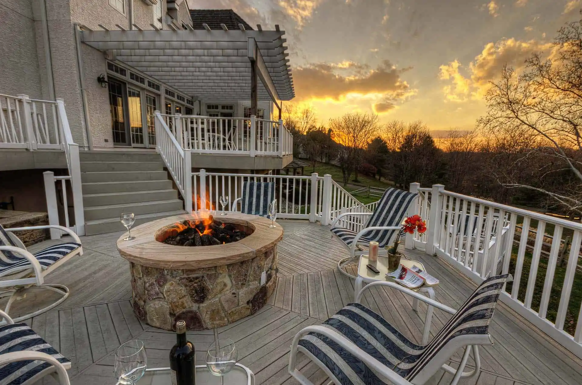 A serene deck with chairs and a fire pit, illuminated by the warm glow of a sunset in the background.