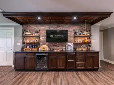 A home bar with dark wood cabinets, a brick backsplash, and liquor shelves is elegantly styled for outdoor living Delaware County PA. A TV showcasing 