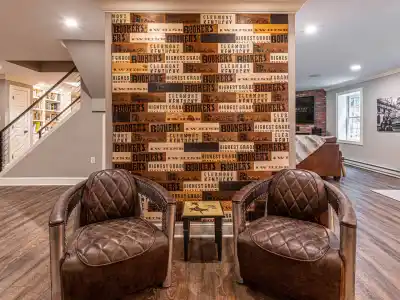 Two brown leather armchairs face a wall adorned with a collage of wooden boards featuring text like 