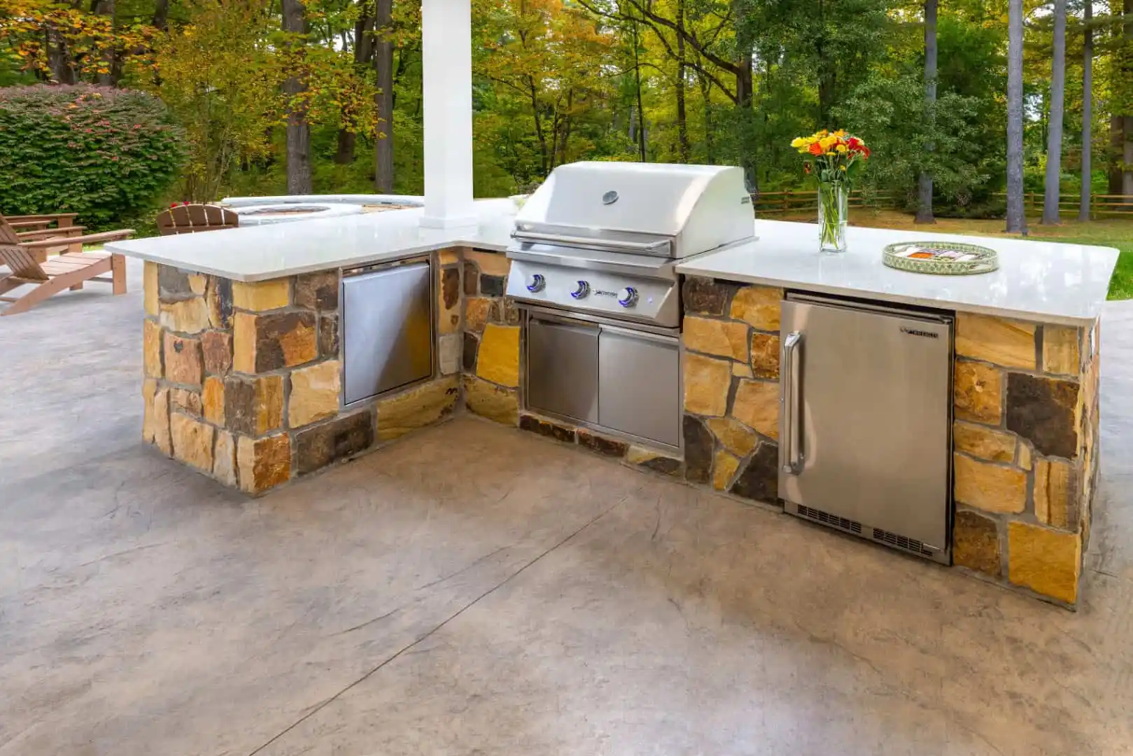 Discover the perfect outdoor living space in Delaware County, PA, with this elegant kitchen. Featuring a stone and stainless steel setup, it includes a gas grill, refrigerator, and shelving. Surrounded by lush greenery, it epitomizes top-tier landscaping services available in the area.