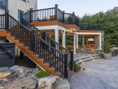 Outdoor living in Delaware County, PA shines with this multi-level patio featuring a staircase to a covered seating area. Enjoy the stone fireplace and elegant lighting fixtures, all expertly designed through our hardscaping services and surrounded by lush greenery and rocks.