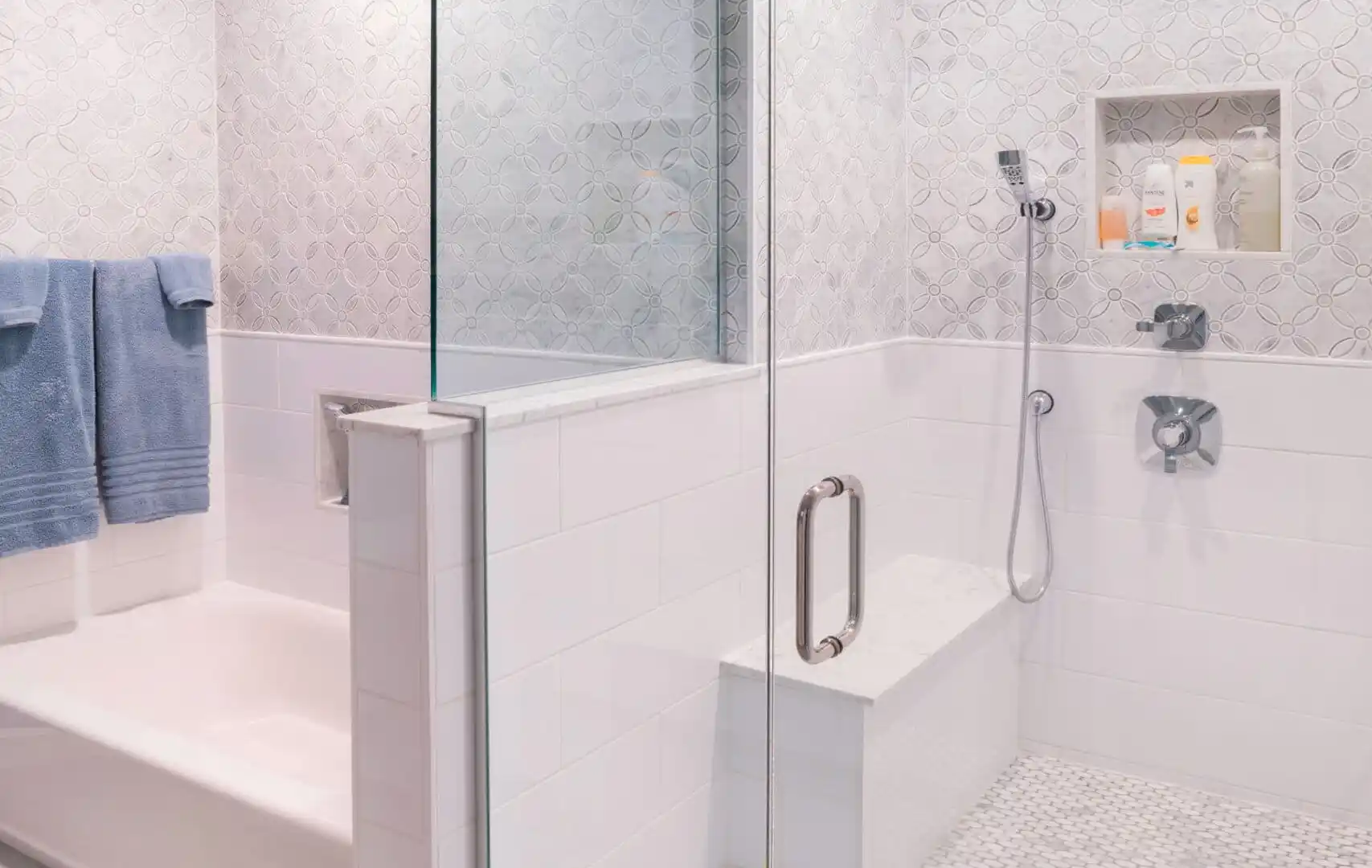 A modern bathroom features a walk-in glass shower with a built-in bench and rainfall showerhead. The walls have a textured design, and the floor has a small hexagonal tile pattern. With its seamless blend of indoor elegance and outdoor living, this space feels like an oasis.