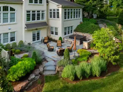 Nestled in Delaware County, PA, this elegant backyard showcases the best of outdoor living with a stone patio, comfortable furniture, and a soothing hot tub. The lush landscaping complements the two-story house's numerous windows and pristine lawn, creating a serene and inviting atmosphere.