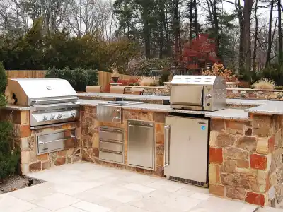 Discover the perfect outdoor living space in Delaware County, PA, with a stone-counter kitchen featuring two stainless steel grills and storage cabinets. Nestled among trees with a patio area, this setup offers a cozy and functional environment for alfresco cooking.
