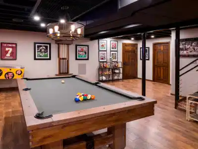 A basement game room showcases a wooden pool table with balls perfectly set up. Sports memorabilia, framed jerseys, and photos adorn the walls. A classic pinball machine sits in the corner, enhancing this cozy hideaway. Experience expert hardscaping services in Delaware County, PA to transform your space.