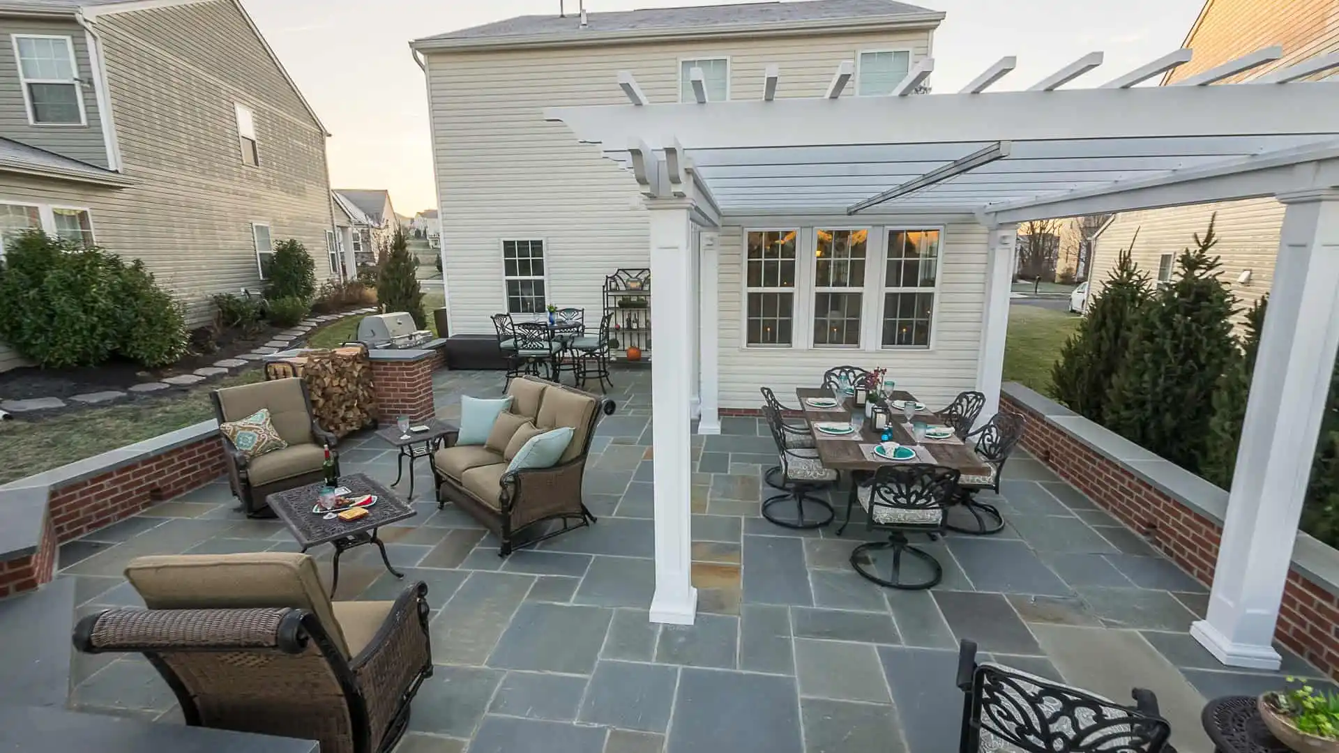 Enjoy the perfect outdoor living space in Delaware County, PA, with a backyard patio featuring a pergola, cushioned seating, and a dining set. Surrounded by brick walls and slate tiles, it's an inviting haven for those seeking premium hardscaping services in the area.