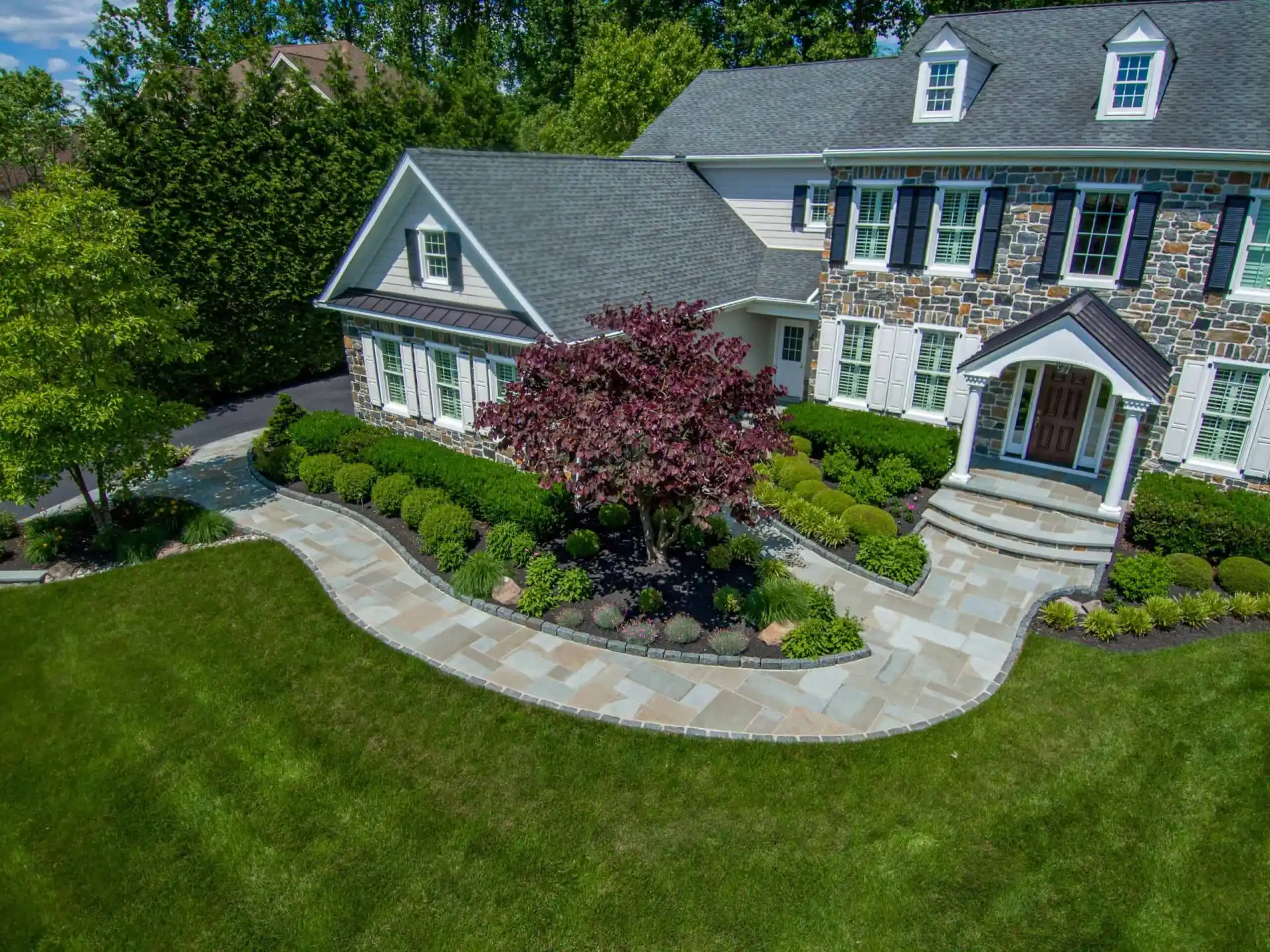 Nestled in Delaware County, PA, this elegant backyard showcases the best of outdoor living with a stone patio, comfortable furniture, and a soothing hot tub. The lush landscaping complements the two-story house's numerous windows and pristine lawn, creating a serene and inviting atmosphere.